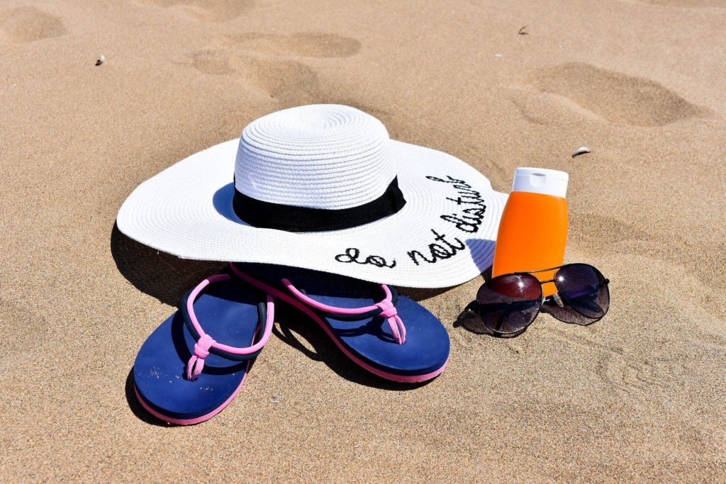 kapelusz przeciwsłoneczny, okulary przeciwsłoneczne, klapki, krem leżące na plaży